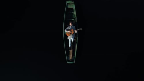 An Adult Man Lies in a Wooden Green Authentic Boat and Plays the Guitar