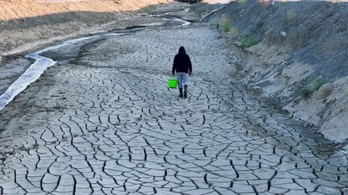 Person Walking Through Cracked Earth Riverbed During Drought