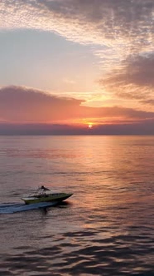 Vertikales Video-Sportboot segelt bei Sonnenuntergang zum Hafen, bewölkter Abend