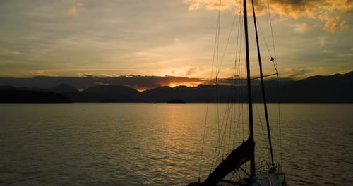 Beautiful aerial drone subtle traveling up of sail boat in calm ocean with amazing orange sunset wit