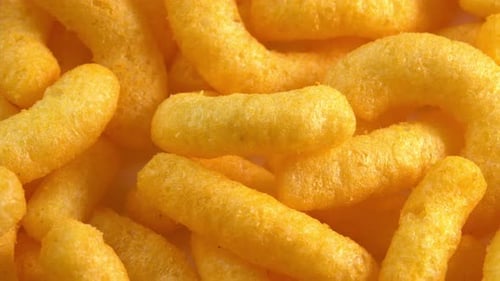 Käsige Maisstäbchen drehen sich auf dem Teller in der Nähe des Seitenlichts. Knuspriger Käsesnack. Knuspriger, flauschiger Mais