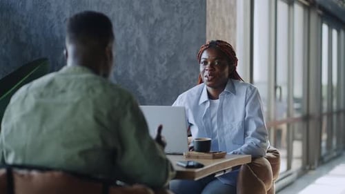 Two Colleagues in Formal Wear Drinking Coffee and Discussing Work Using Modern Gadgets in a Cafe