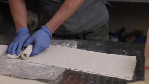 Hands Unrolling White Fabric Material on Table