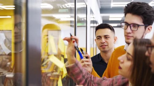 Business Team Brainstorm Writing Ideas on Paper Sticky Notes and Post It on Glass Wall Startup