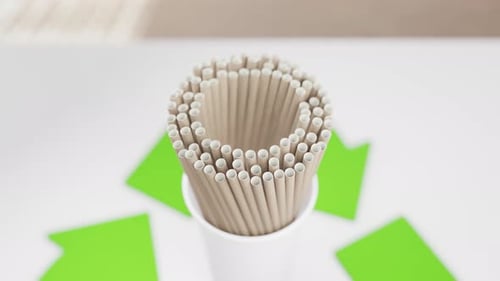 A cup filled with paper straws center within a vibrant green recycling
