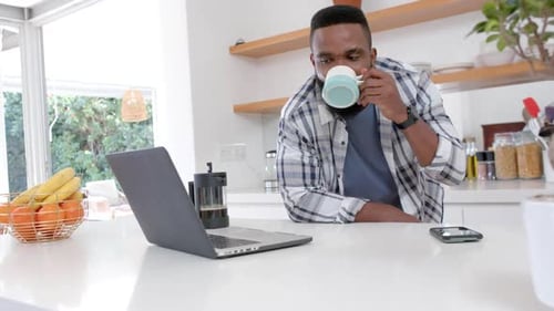 Adult Drinks Coffee and Uses Laptop in Kitchen