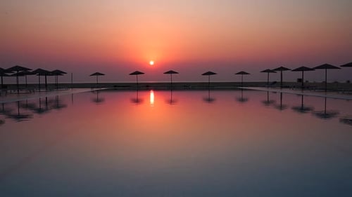 Perfect red sunset view from tropical hotel resort lounge with infinity pool, beach umbrellas and th
