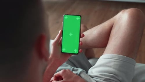 Caucasian Man Using Smartphone in Vertical Mode with Green Mockup Screen Doing Swiping Scrolling