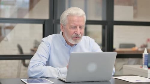Old Businessman Chatting Online on Laptop while Sitting in Office