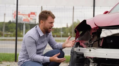 Distressed Man Kneels Beside Damaged Car After Accident