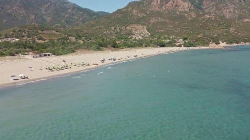 Aerial Drone Slide View of Tropical Sea with People Swimming and Umbrellas at Beach. Mountains on Ba
