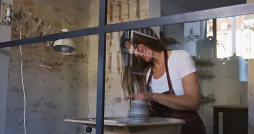 Creative female artisan skillfully shaping clay in her sunny pottery workshop