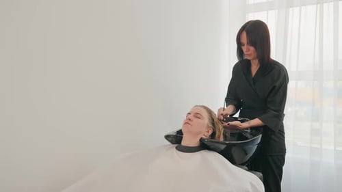 Hairdresser working in salon washing woman's long hair