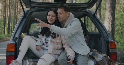 Slow Motion of Man and Woman Talking Pointing at Beautiful Forest Sitting in Car Enjoying Road Trip
