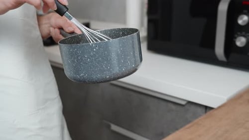 The cook, while stirring the contents of the saucepan, carries it and places it on a double boiler