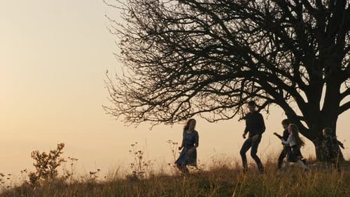 Family Enjoys Sunset Near Tree on Hillside