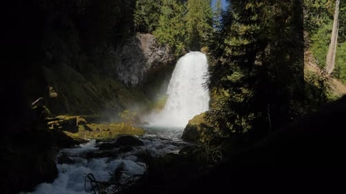 Slow motion, wide shot of a waterfall in the forest with sun beaming through