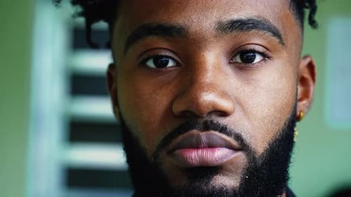 Portrait of a black young man staring at camera with solemn serious expression, close-up facial