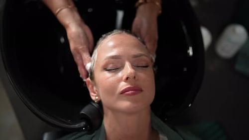 Top View of Unrecognizable Hairstylist Foaming Shampoo on Long Blonde Hair of Beautiful Female