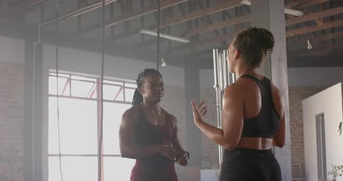 Discussing workout routine, two women in gym wearing athletic clothing
