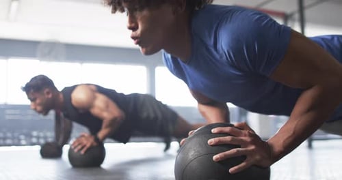Men doing push-ups on medicine balls during intense gym workout session