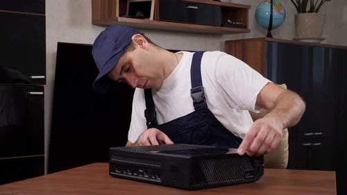 A Male Handyman Repairs a Game Console at a Table From Using a Screwdriver