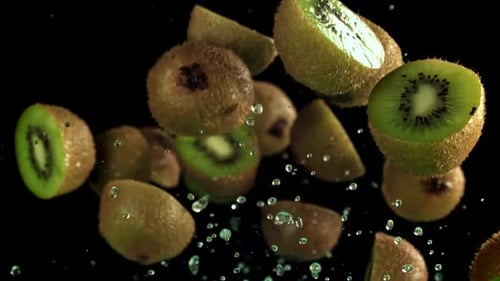 Fresh kiwi fruit slices falling against black background