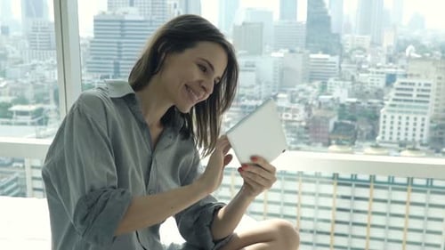 Woman Using Tablet on Bed with City View
