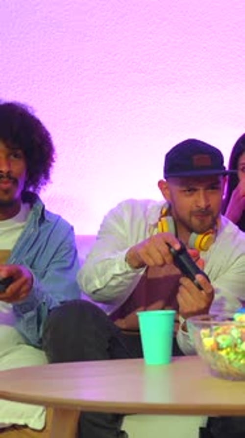 Party für Erwachsene. Attraktive junge Männer sitzen auf dem Sofa und spielen Videospiele mit Popcorn. Mit der Freude