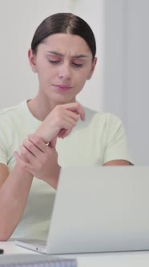 Young Woman Massaging Wrist in Front of Laptop