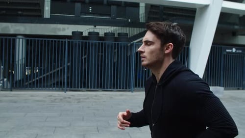 Focused young sportsman running on urban street cardio training in slow motion