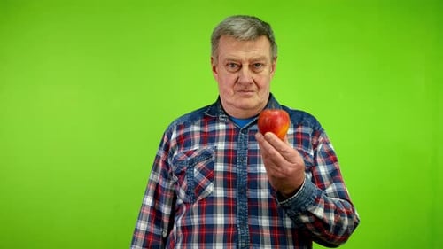 Un homme âgé positif montre une pomme mûre et lève le pouce pour affirmer les bienfaits des fruits