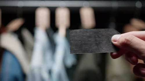 Hand Holding a Small Black Tag Near Clothes