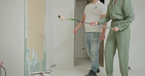 Woman Paints Wall with Roller as Man Watches