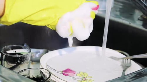 Washing Dishes With Rubber Gloves in Kitchen Sink