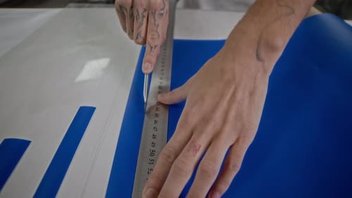 Hands Cutting Blue Material with Knife and Ruler