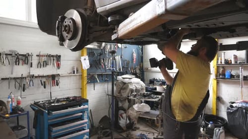 Auto Mechanic Working Underneath a Lifting Vehicle at Garage Professional Bearded Repairman