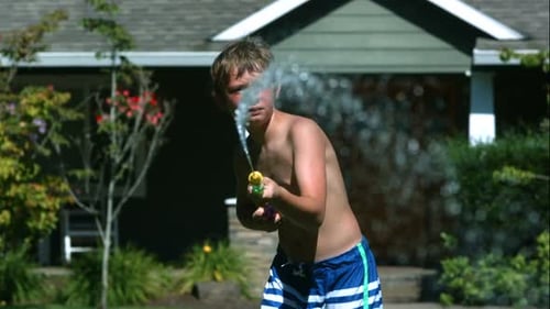 Boy Plays with Water Gun in Summer Backyard