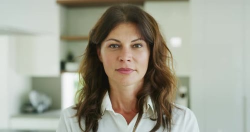 Authentic close up shot of an attractive happy brunette woman is smiling in camera in a kitchen at