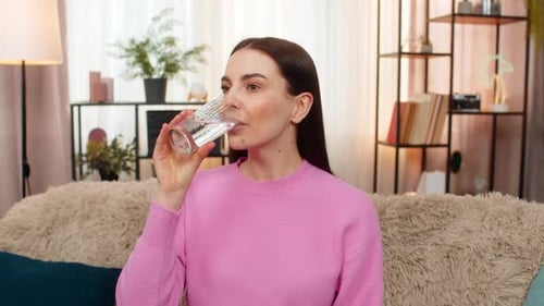 Woman Drinking Glass of Water, Smiling on Couch