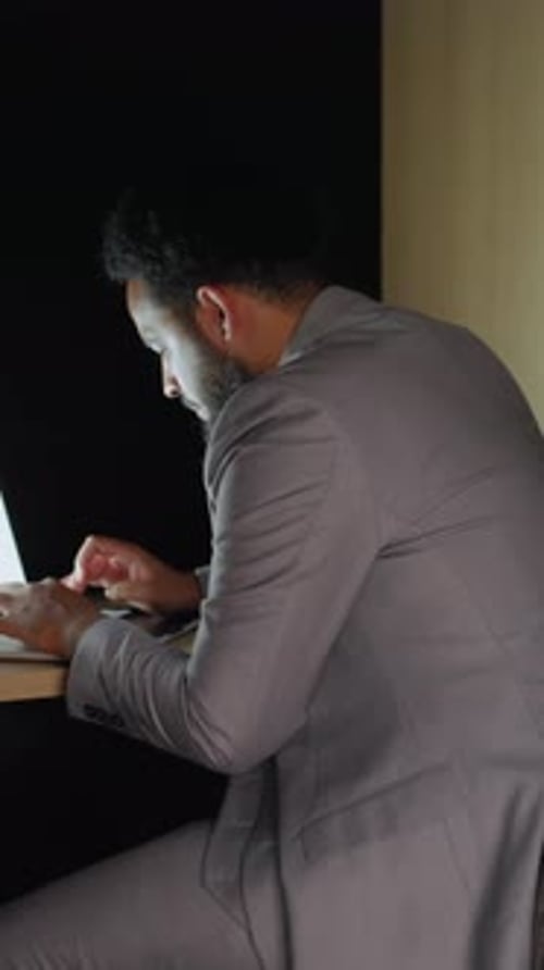 Man in Suit Typing on Laptop in Office Booth