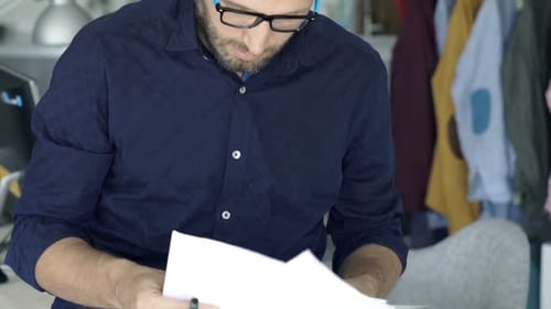 Young entrepreneur standing at home analyzing financial documents and making notes