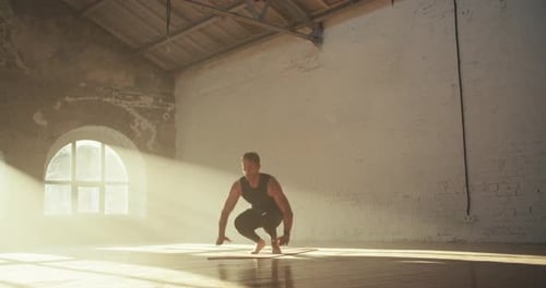 Un homme vêtu d'un uniforme sportif d'été noir fait un exercice de burpee sur le tapis rouge dans le Sunny Brick Hall