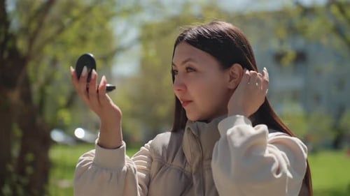 Individual Adjusting Makeup Using Mirror Surrounded By Greenery Woman Carefully Perfecting Her