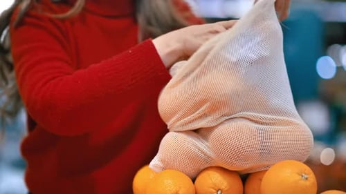 Mujer recogiendo naranjas en una bolsa reutilizable en una tienda. Temáticas del Día de la Tierra y la Ecología
