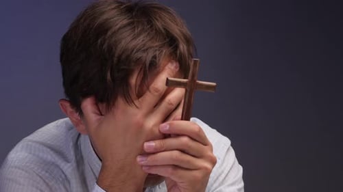 Man Holding Cross and Praying with Hands Covered