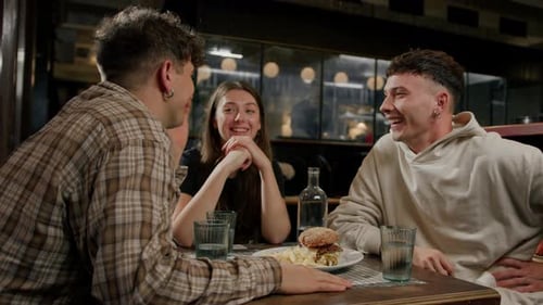 Wide shot - a group of friends chatting at a table in a restaurant, eating a burger and french fries