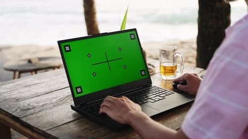 Man Works on Laptop with Green Screen at Seaside Cafe Freelancer Types Uses Chroma Key Display