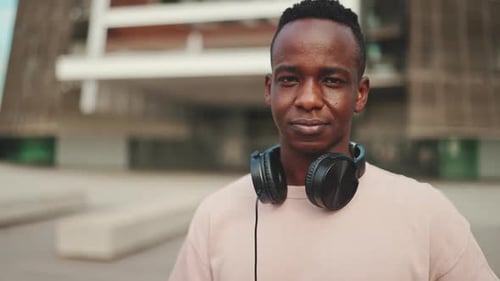 Clouse up, smiling young student stands outside of university in headphones