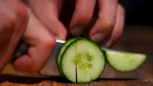 Close up of a male hand cutting a pre cut cucumber into multiple pieces